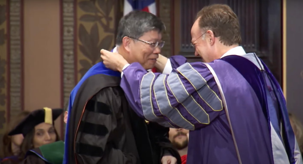 President DeGioia, dressed in a purple commencement robe, gives an award to another professor on the Spring Faculty Convocation stage.